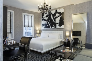 A hotel room with a large bed, a desk, a chair, a TV, and a chandelier. - Square Hotel at Times Square (New York)