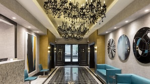Un vestíbulo de hotel con piso de diseño en blanco y negro, una araña, asientos azules y obras de arte en las paredes.