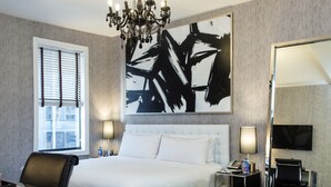 Una habitación de hotel moderna con una cama grande, una araña, un cuadro, un escritorio y un televisor.
