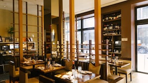 Interior de restaurante con separadores de madera, mesas, sillas y una estantería para vinos.