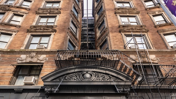 Un edificio con entrada negra, escaleras de emergencia y un letrero que indica un hidrante.