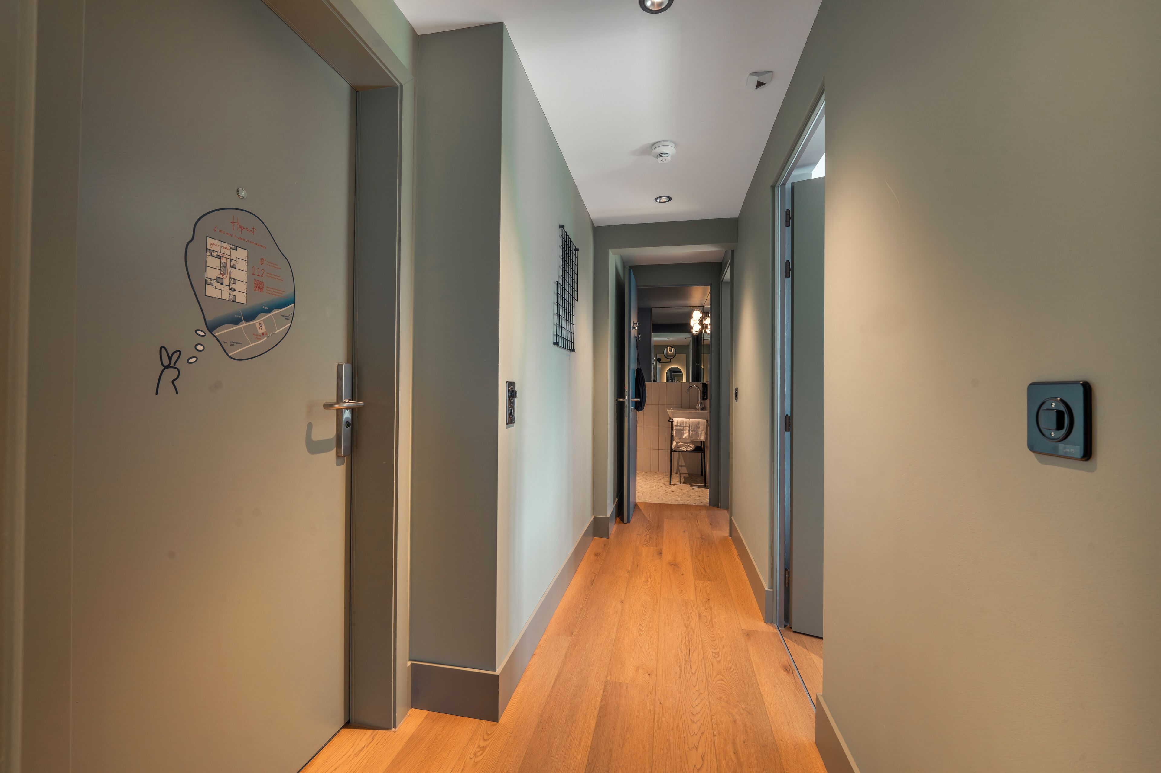 Un pasillo con piso de madera, una puerta con un mapa y un interruptor de luz en la pared.