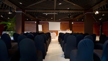 Une salle de conférence avec des rangées de chaises, un écran de projection et un pupitre.
