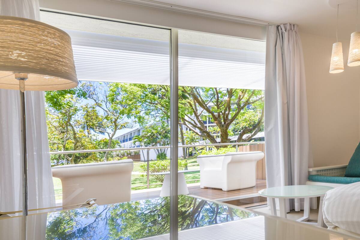A hotel room with a glass-enclosed balcony, a bed, a small table, and a chair.