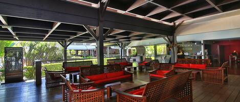 A covered outdoor seating area with wooden furniture and a view of the surrounding greenery.