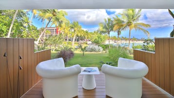Una terraza con dos sillas blancas y una mesa pequeña, con vista a una playa y palmeras.