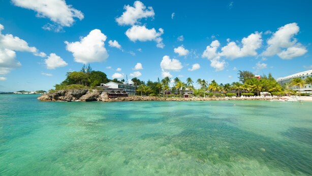 Una isla tropical con aguas turquesas cristalinas, un afloramiento rocoso con un edificio y palmeras.