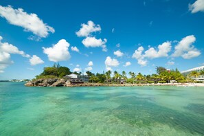 A tropical island with clear turquoise waters, a rocky outcrop with a building, and palm trees. - La Creole Beach Hôtel & Spa (Le Gosier)