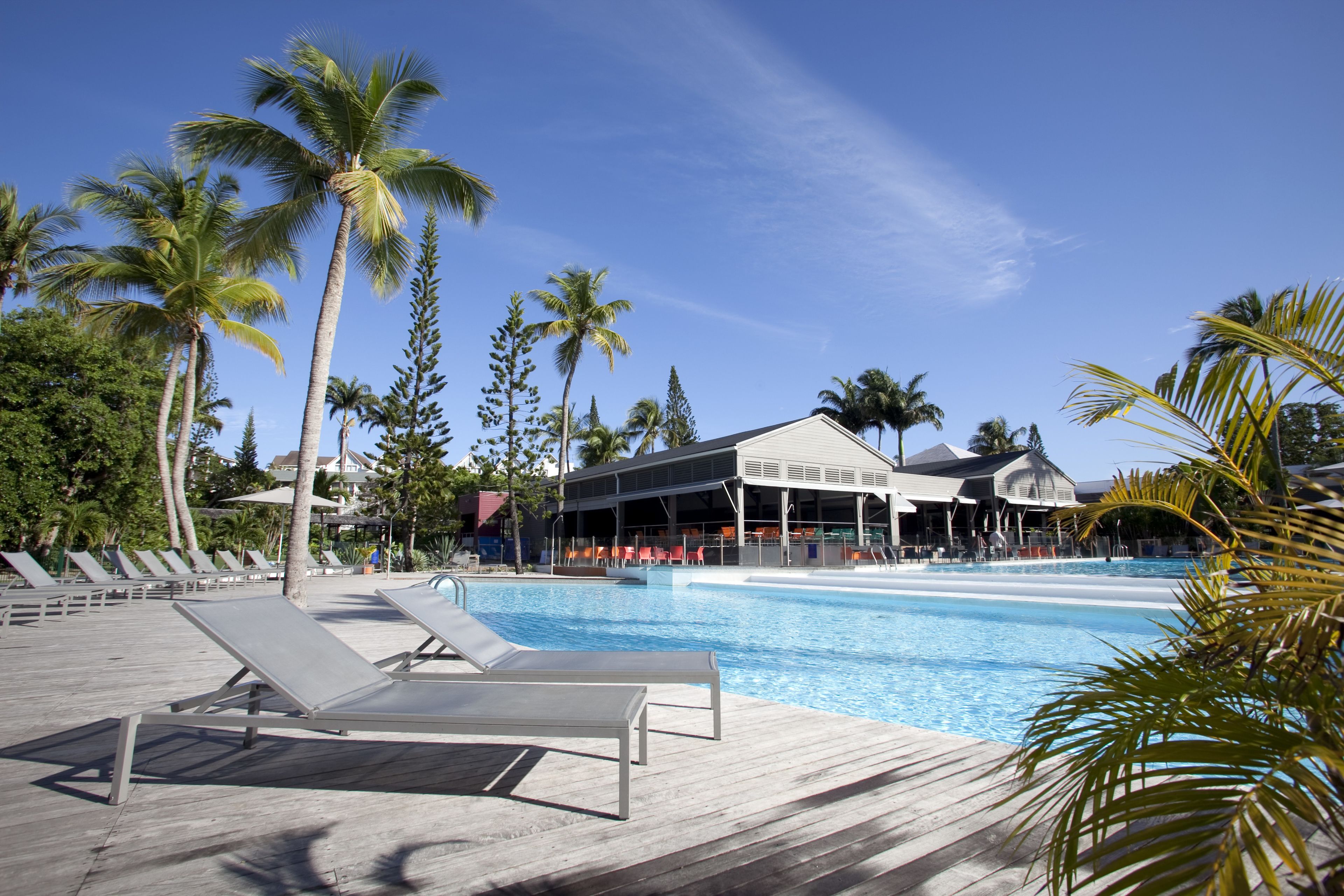 A pool area with lounge chairs, palm trees, and a building with a covered seating area.