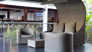 A modern lounge area with wicker furniture, a bar in the background, and a view of the outdoors.