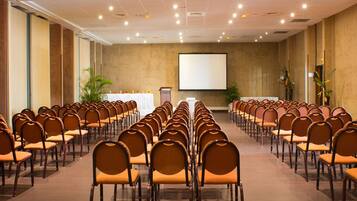 A conference room with rows of chairs facing a projection screen, a podium, and potted plants.