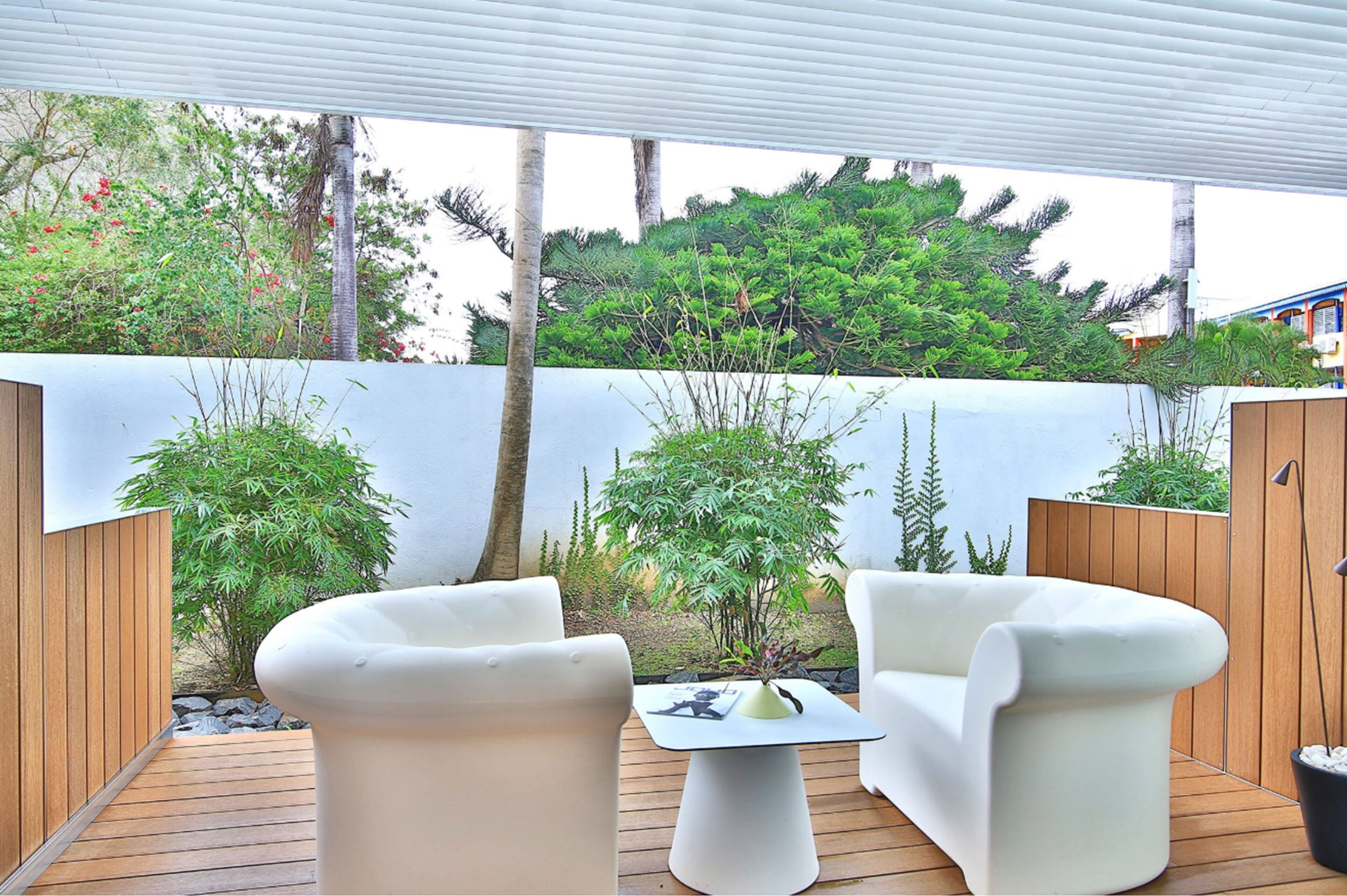 An outdoor patio with wooden flooring, white cushioned chairs, and a small table.