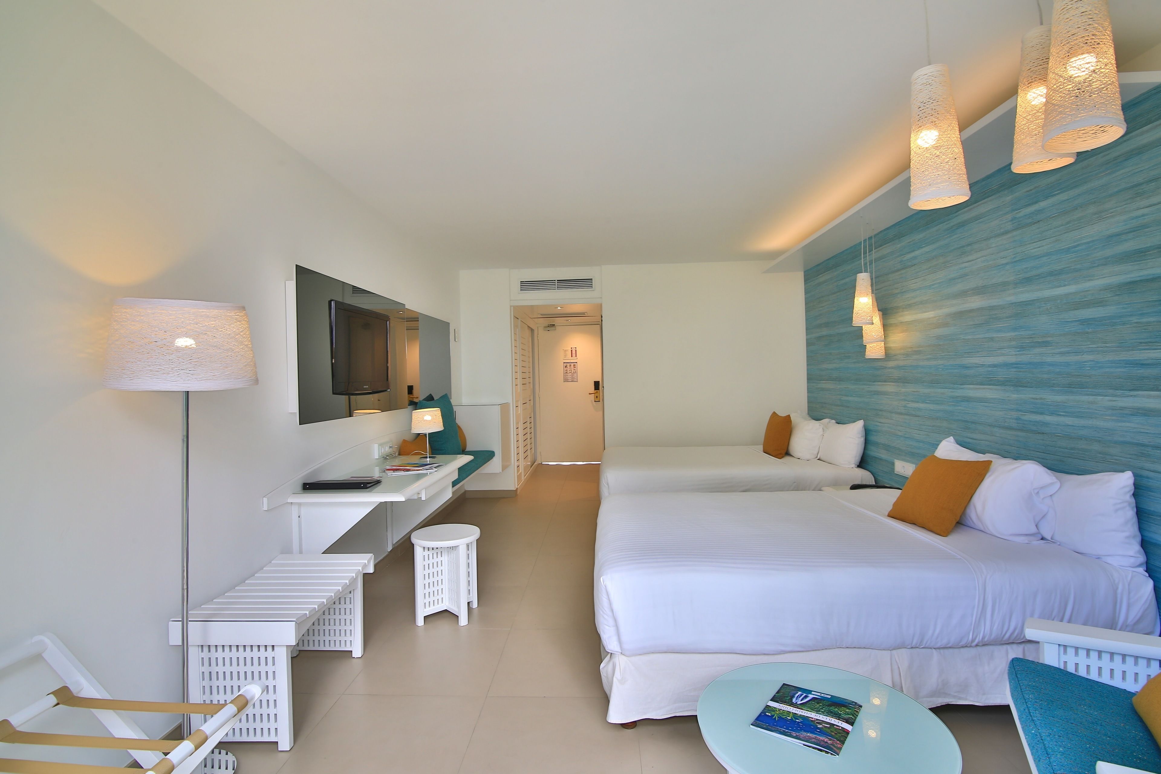 Una habitación de hotel con una cama grande, un escritorio con lámpara, una mesita pequeña y un televisor.