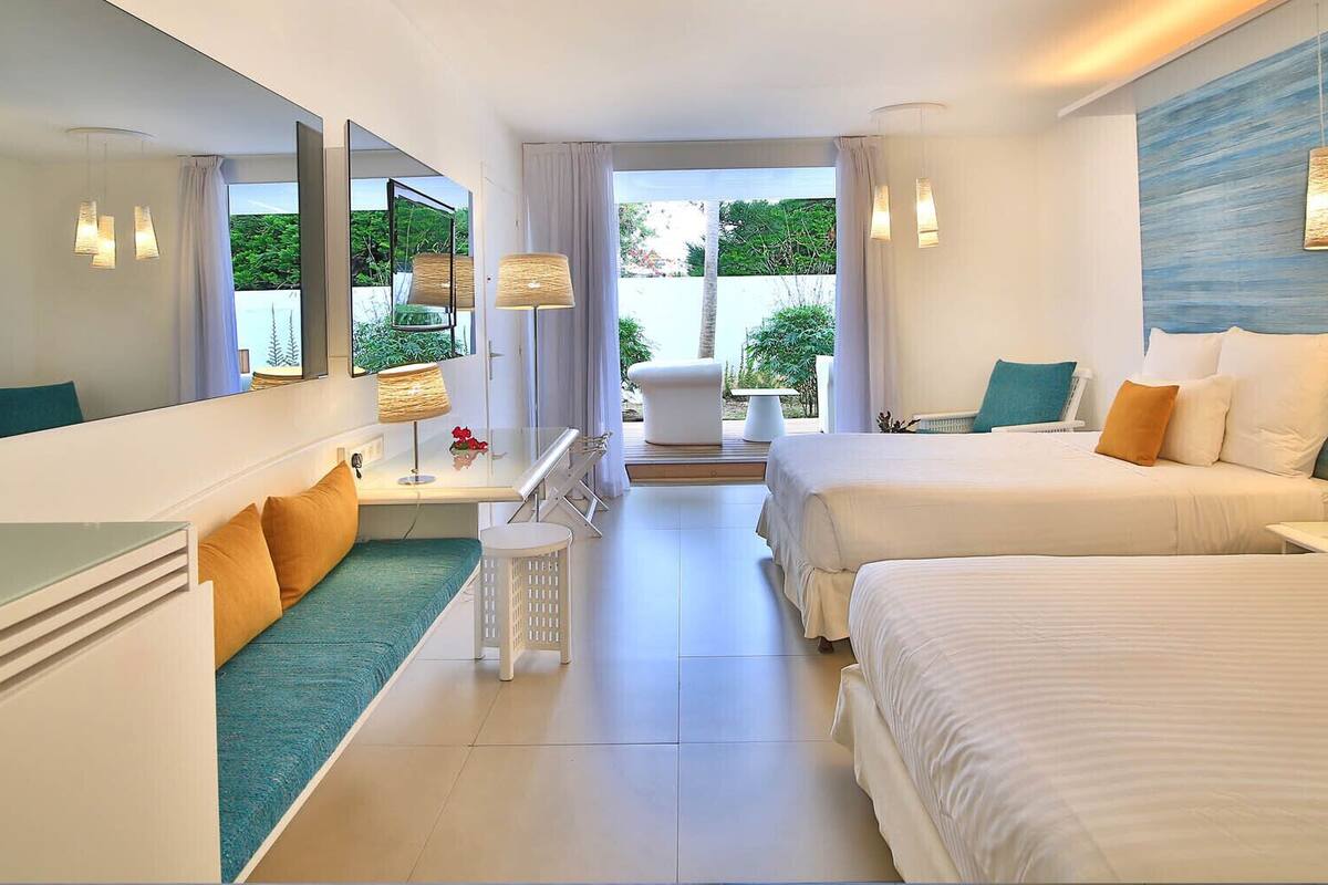 A modern hotel room with two beds, a seating area, and a view of the outdoors.