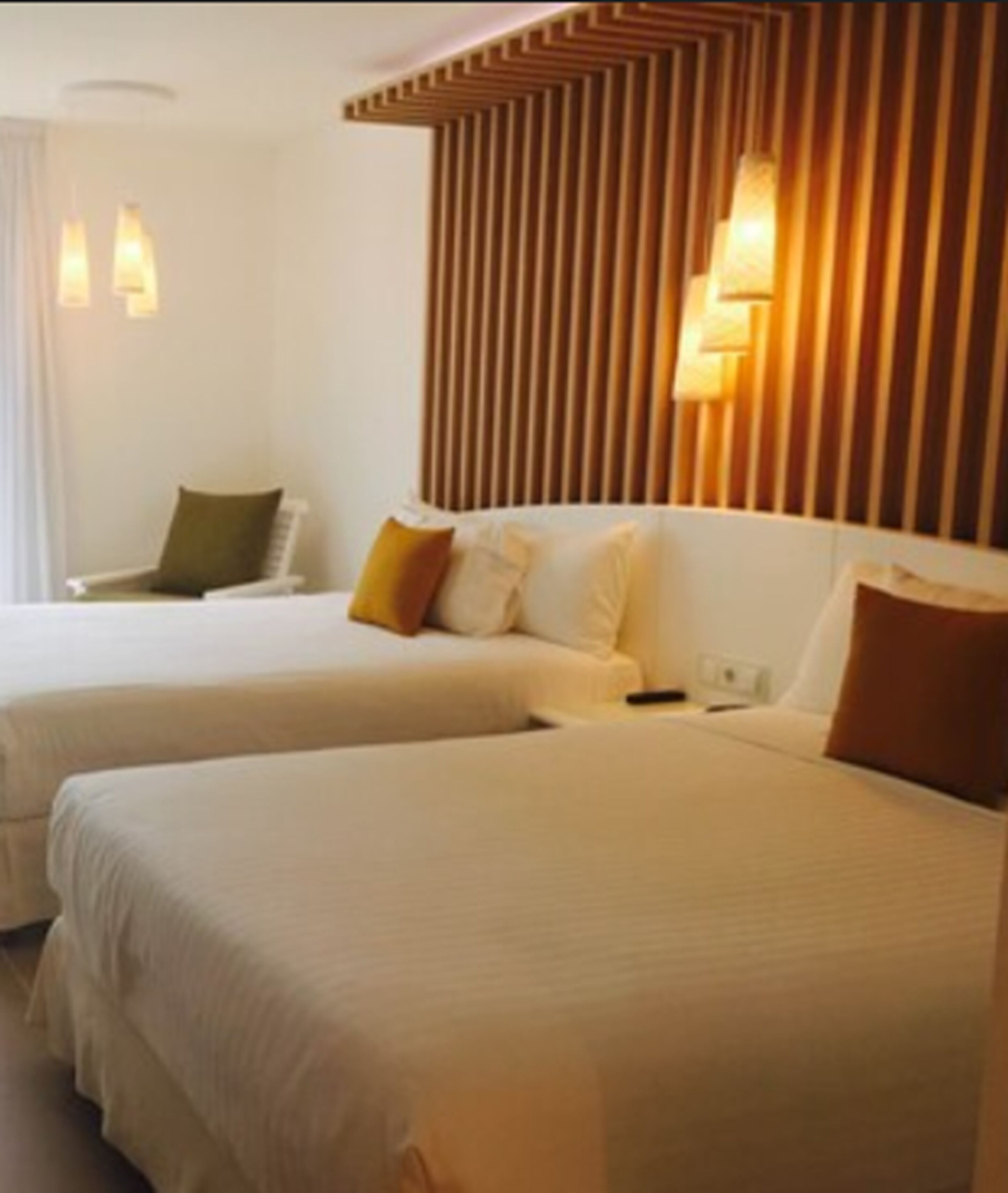 A hotel room with two beds, a wooden slat headboard, and two wall-mounted lamps.