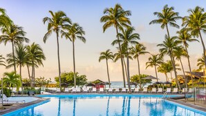 Una piscina con sillas de descanso y palmeras, en un entorno tropical.