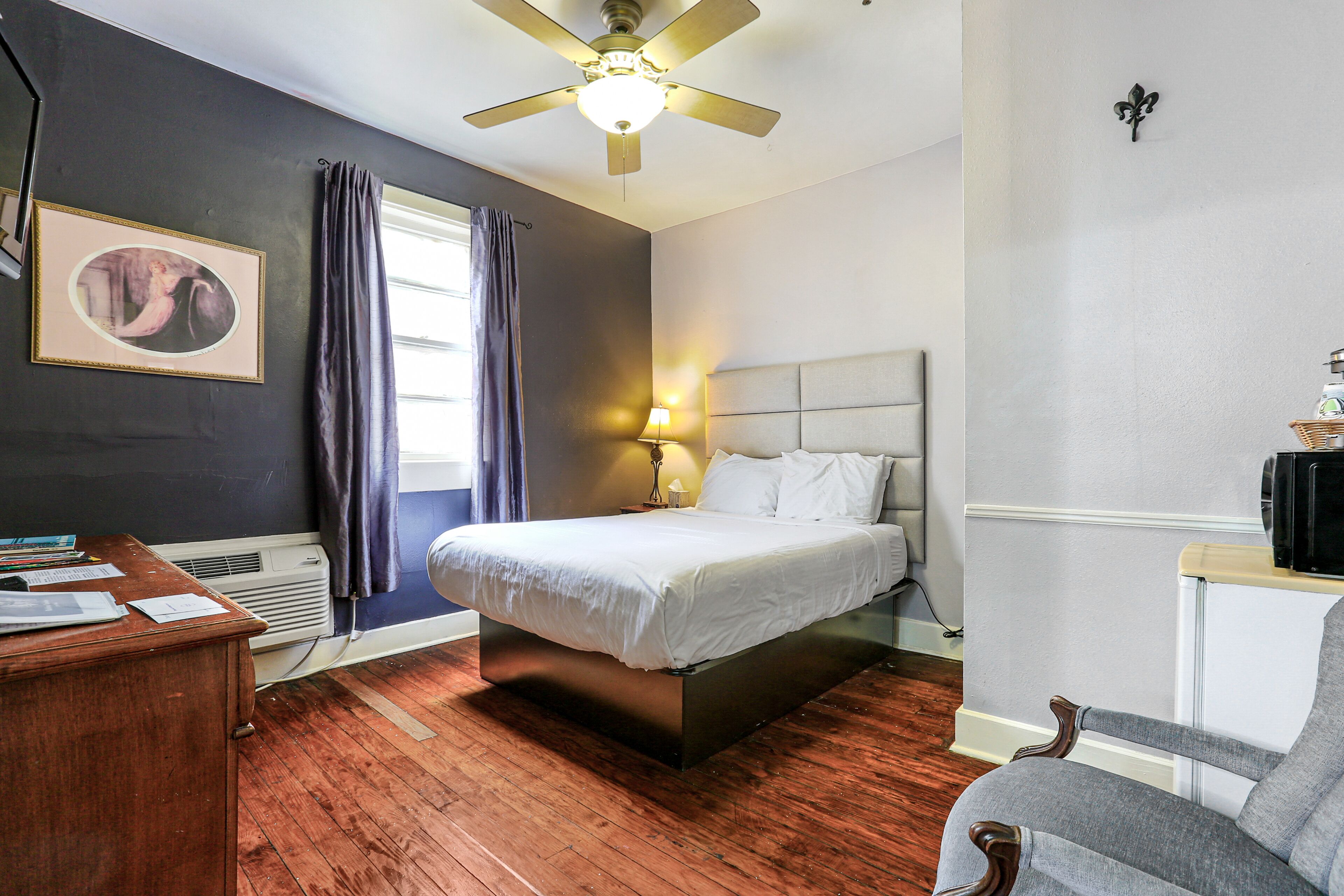 Une chambre à coucher comprenant un lit, un bureau, une chaise, un ventilateur de plafond et une lampe fixée au mur.