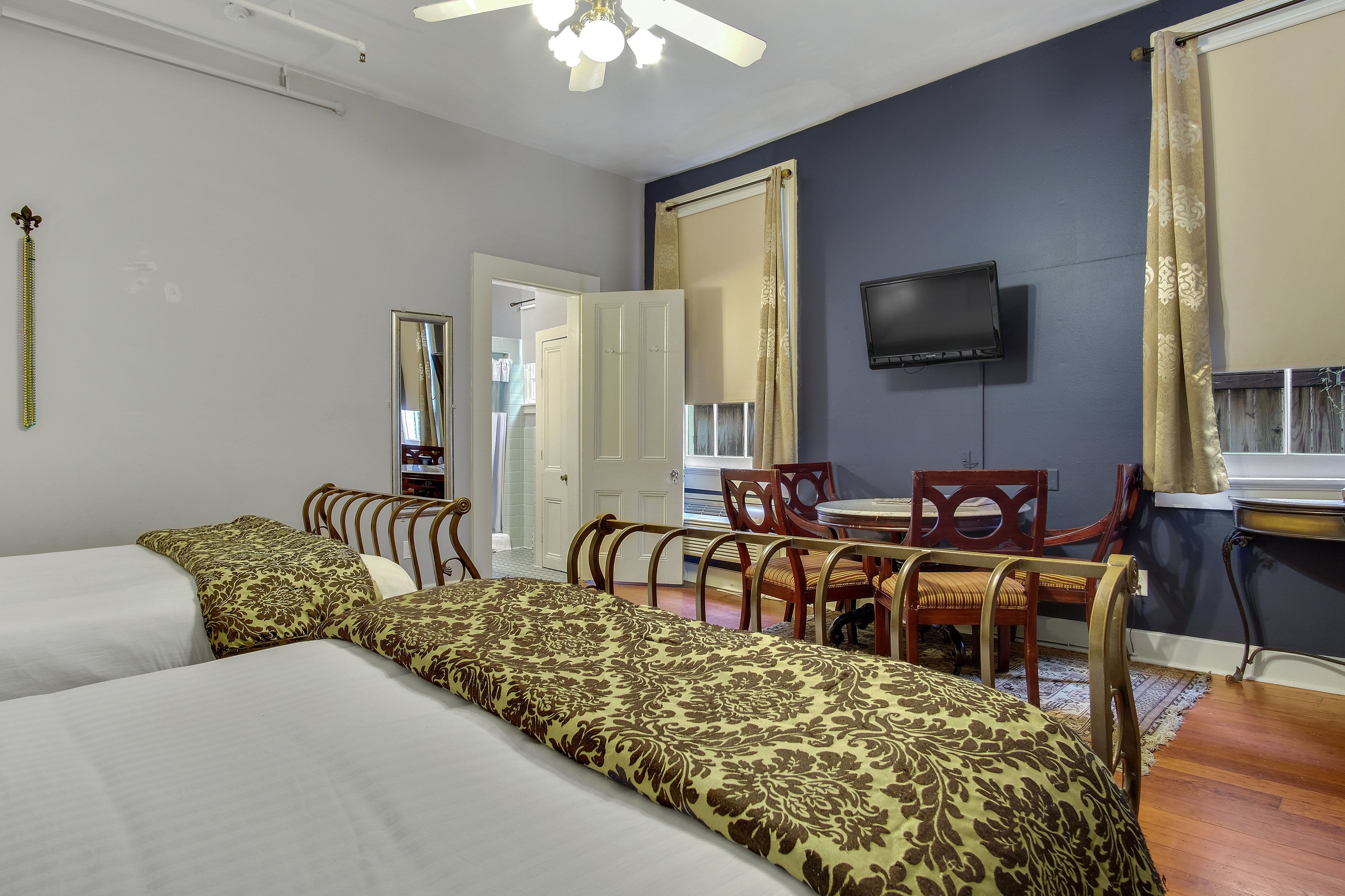 A hotel room with two beds, a dining table with chairs, a TV mounted on the wall, and a window with curtains.