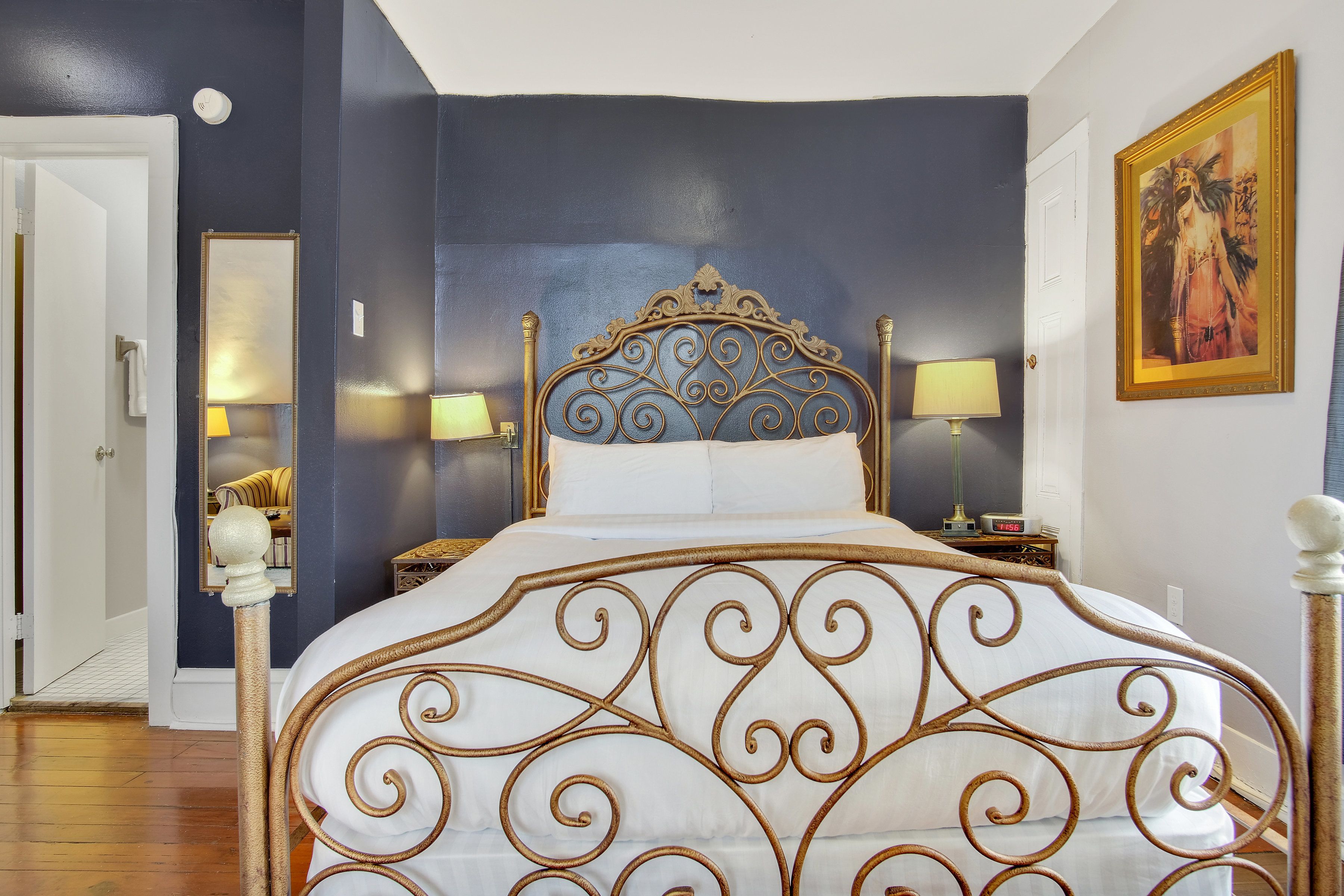 A bedroom with a large bed, a nightstand, a mirror, and a painting on the wall.