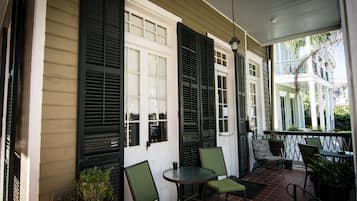Une véranda abritée avec une table et des chaises, une plante en pot et une vue sur un bâtiment doté de volets.