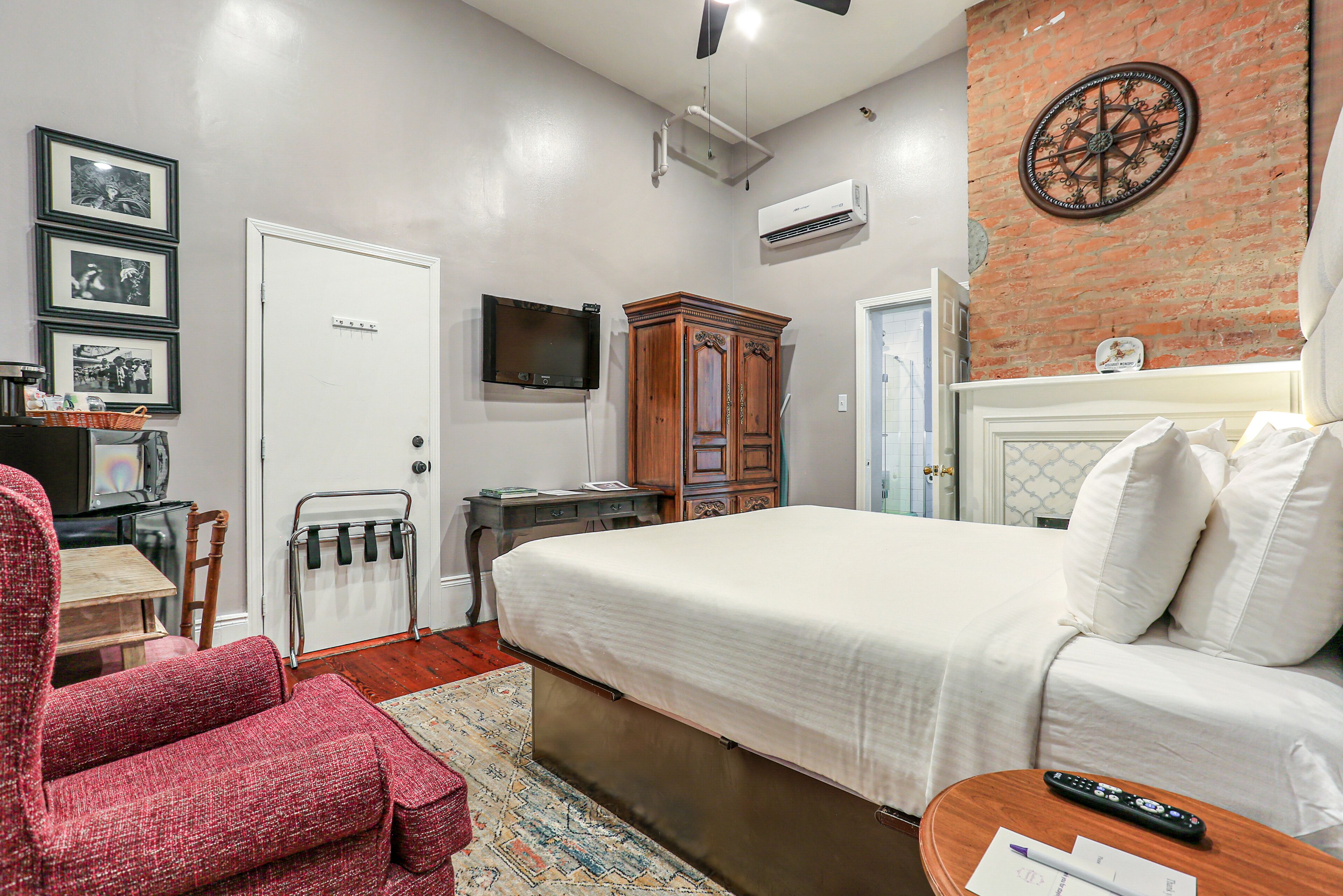 Un dormitorio con cama, televisor, armario, escritorio y sillón rojo.