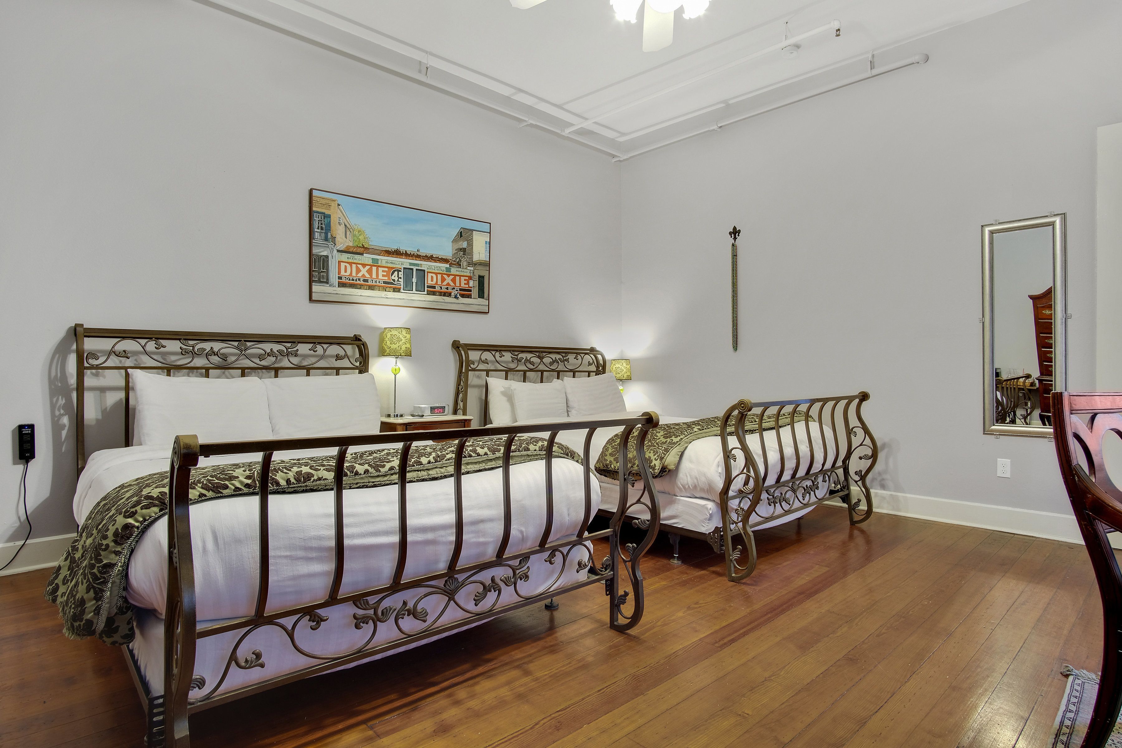 A room with two beds, each with ornate metal headboards, white bedding, and a painting of a building on the wall.