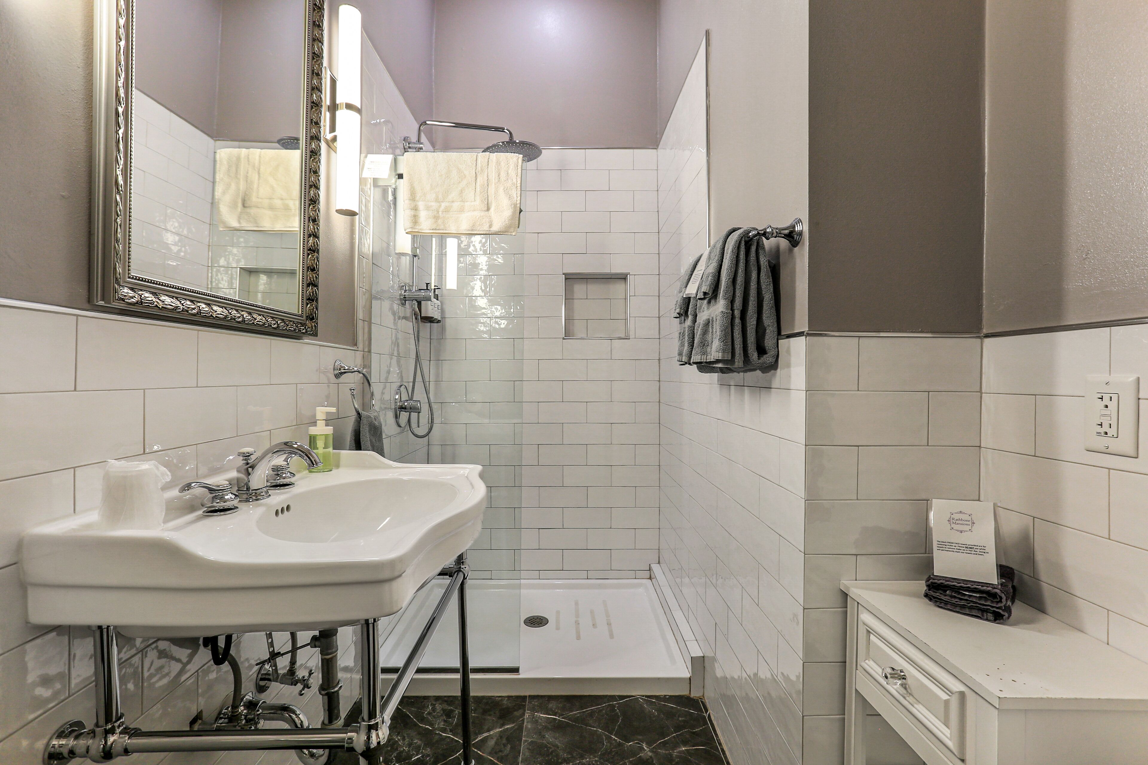 A bathroom with a sink, mirror, towel rack, shower, and a small cabinet.