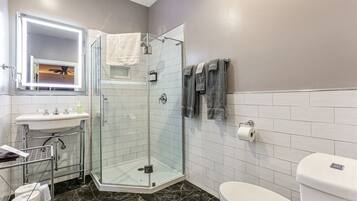 Un baño moderno con ducha de vidrio, lavamanos blanco y retrete.