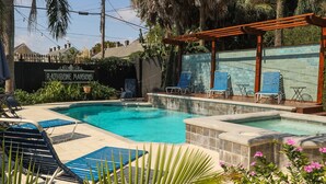 A swimming pool with lounge chairs and a pergola, surrounded by greenery and a brick wall. - Rathbone Mansions (New Orleans)