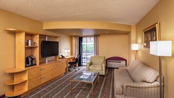 Habitación de hotel con televisión de pantalla plana, muebles de madera, sofá a rayas, mesa de centro de vidrio y vistas al exterior.