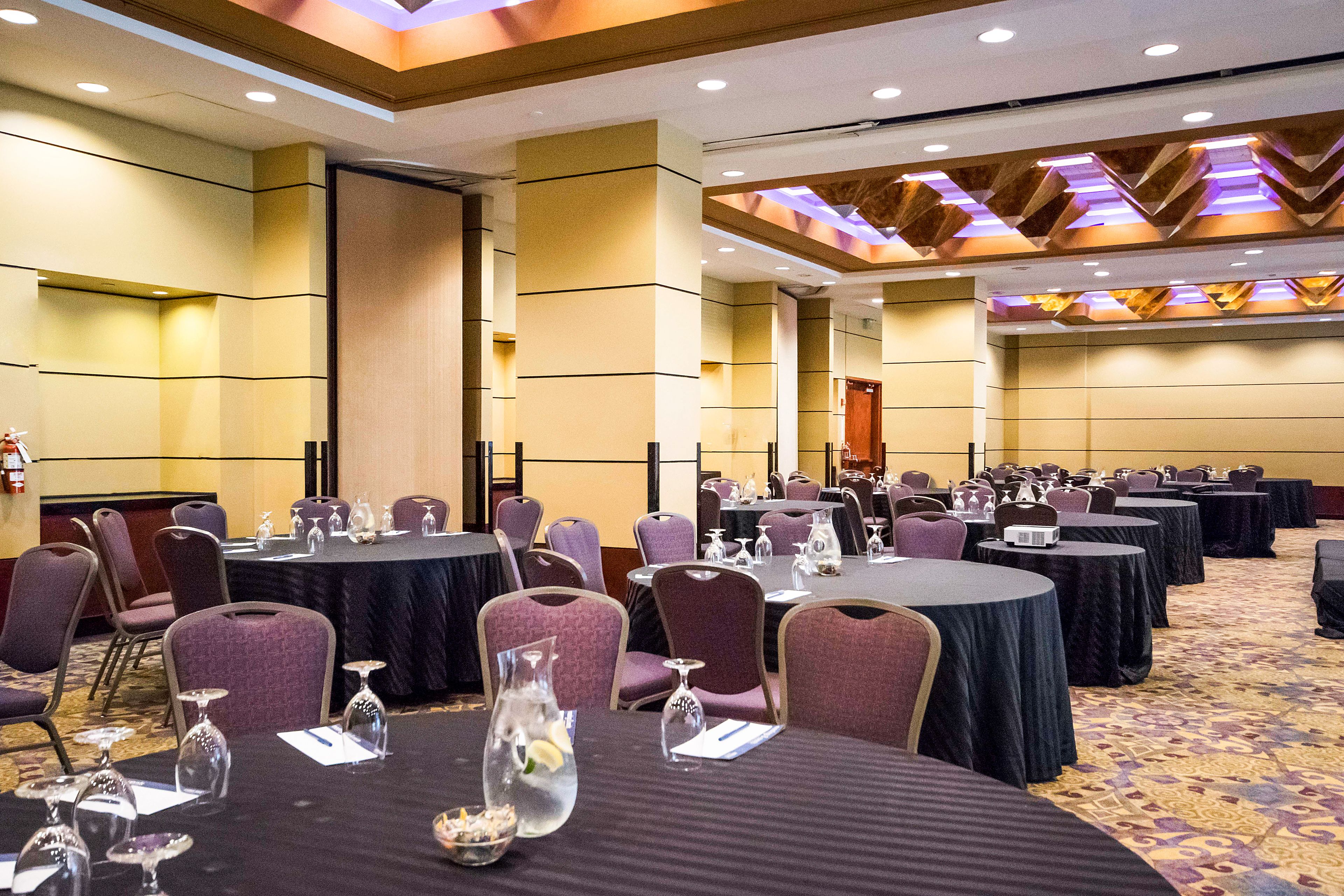 Un salón de conferencias con mesas redondas, sillas y vasos.