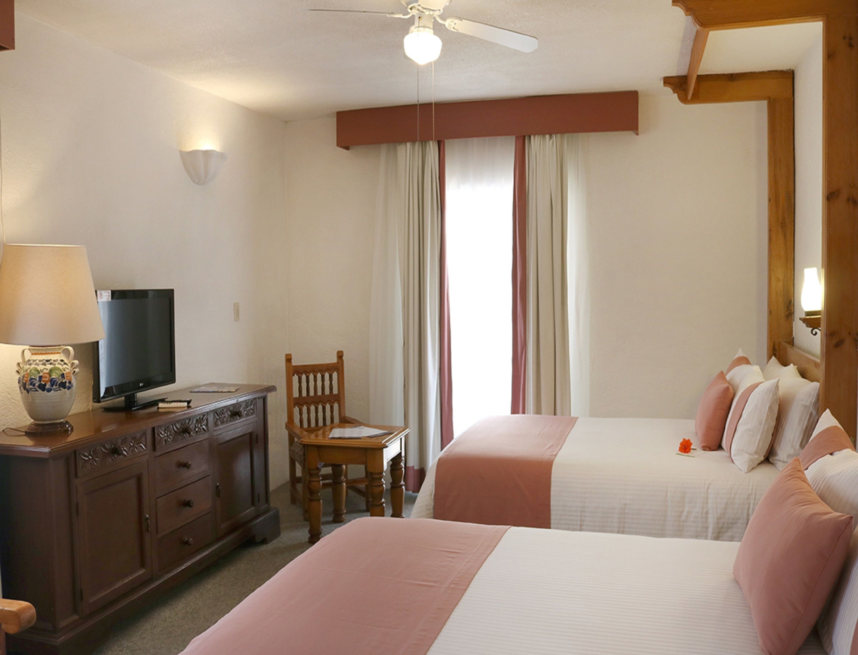 Habitación de hotel con dos camas, un televisor en una cómoda, una silla y un ventilador de techo.