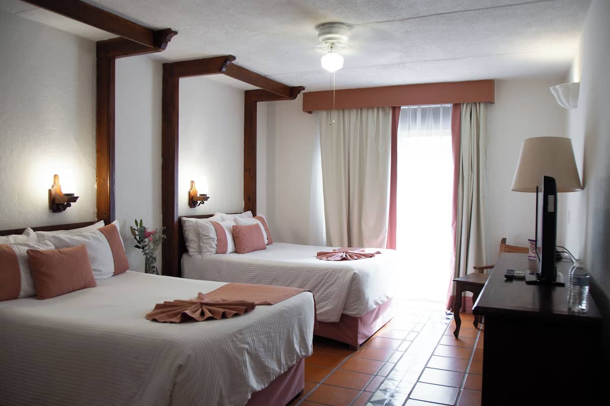 Una habitación de hotel con dos camas, un escritorio con lámpara y una ventana con cortinas.