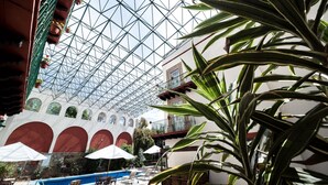 Un espace piscine intérieure doté d’un plafond en verre, d’arcs rouges et de plantes en pot.