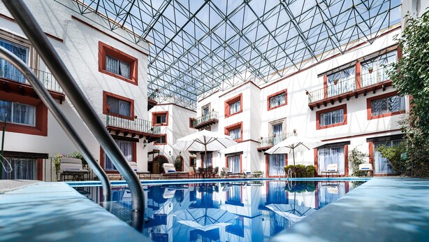 Une piscine intérieure dotée d’un toit en verre, entourée de bâtiments blancs aux accents rouges et agrémentée de balcons.