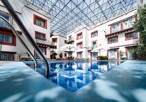 An indoor swimming pool with a glass ceiling, surrounded by white buildings with red accents and balconies. - Hotel Misión Guanajuato (Guanajuato)