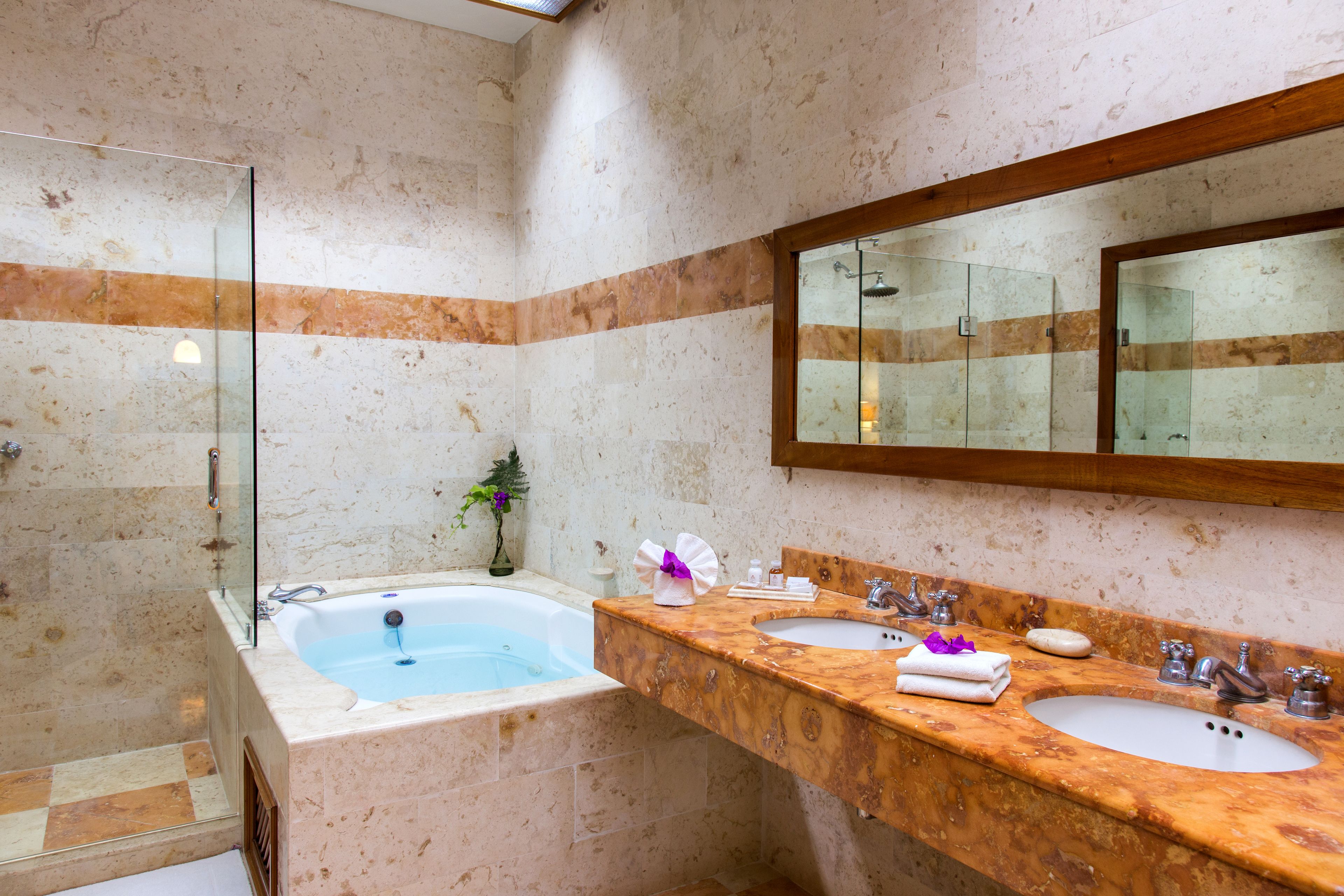 Ein Badezimmer mit einer gläsernen Duschkabine, einer Badewanne und zwei Waschbecken mit Marmorplatten.