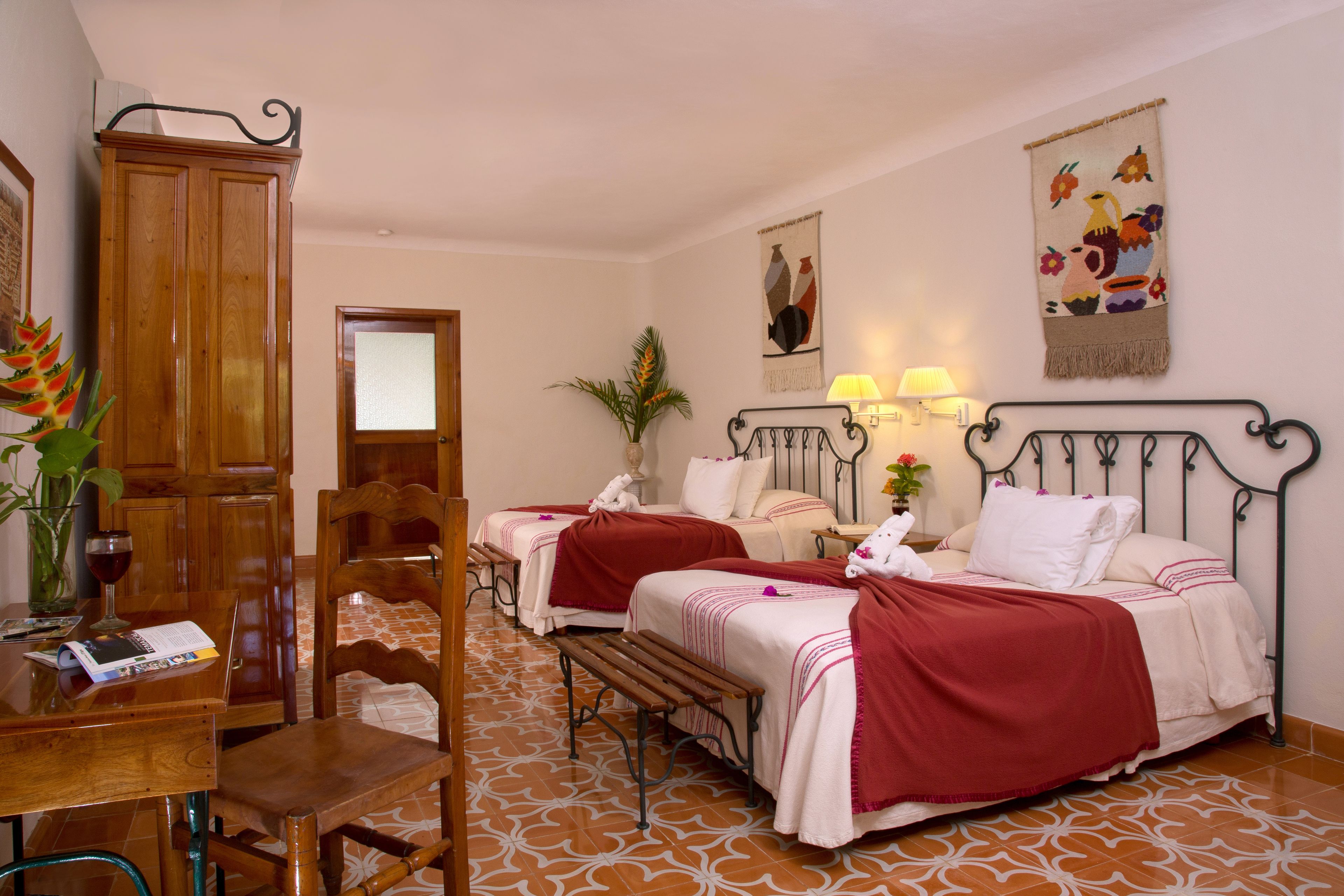 A hotel room with two beds, a wooden cabinet, a dining table with chairs, and a patterned floor.