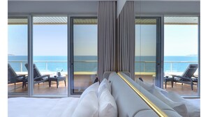 Camera d'albergo moderna con un letto grande, un divano e vista sul mare attraverso finestre a tutta altezza.