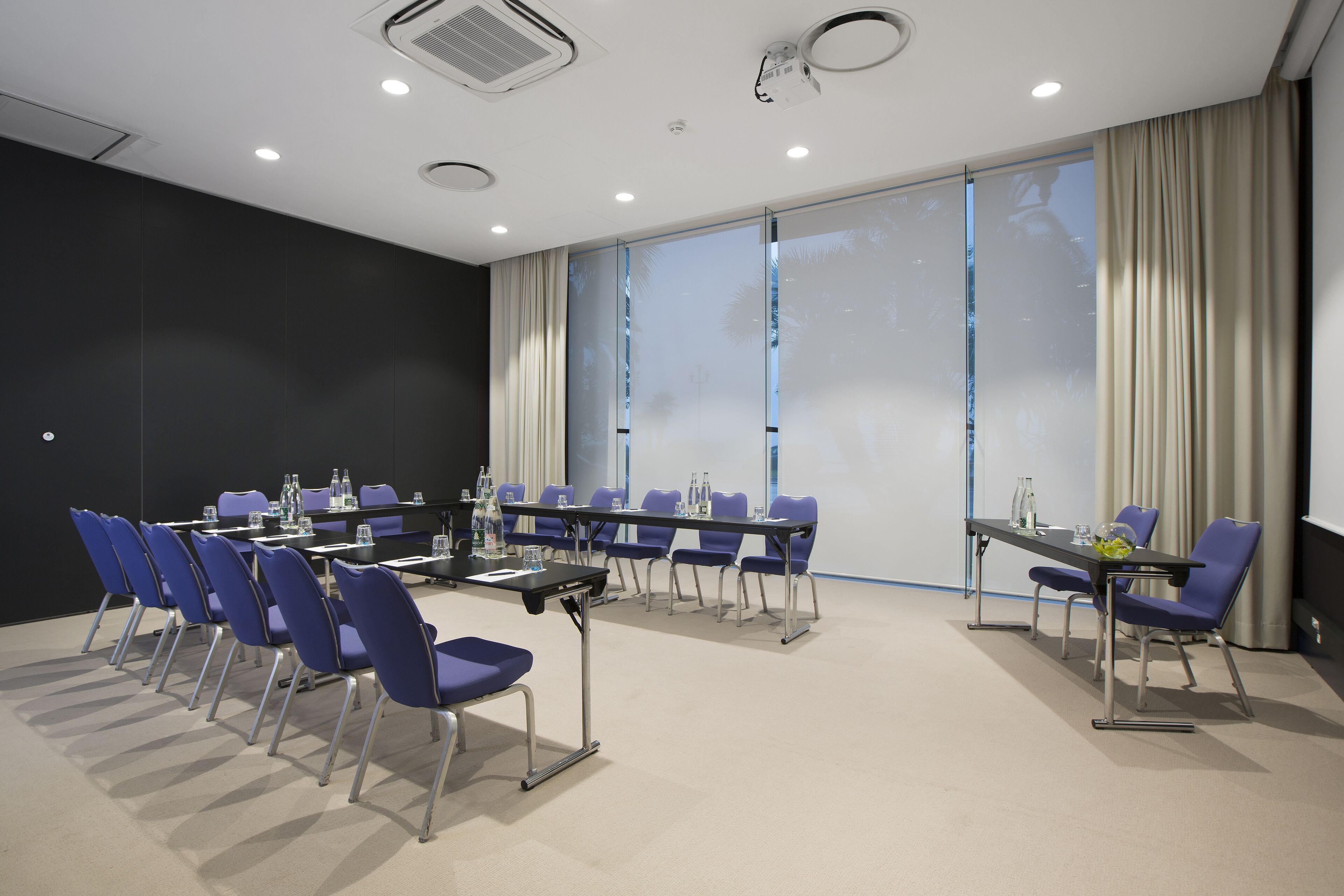 Una sala conferenze con un lungo tavolo, sedie blu e uno schermo per proiezioni.