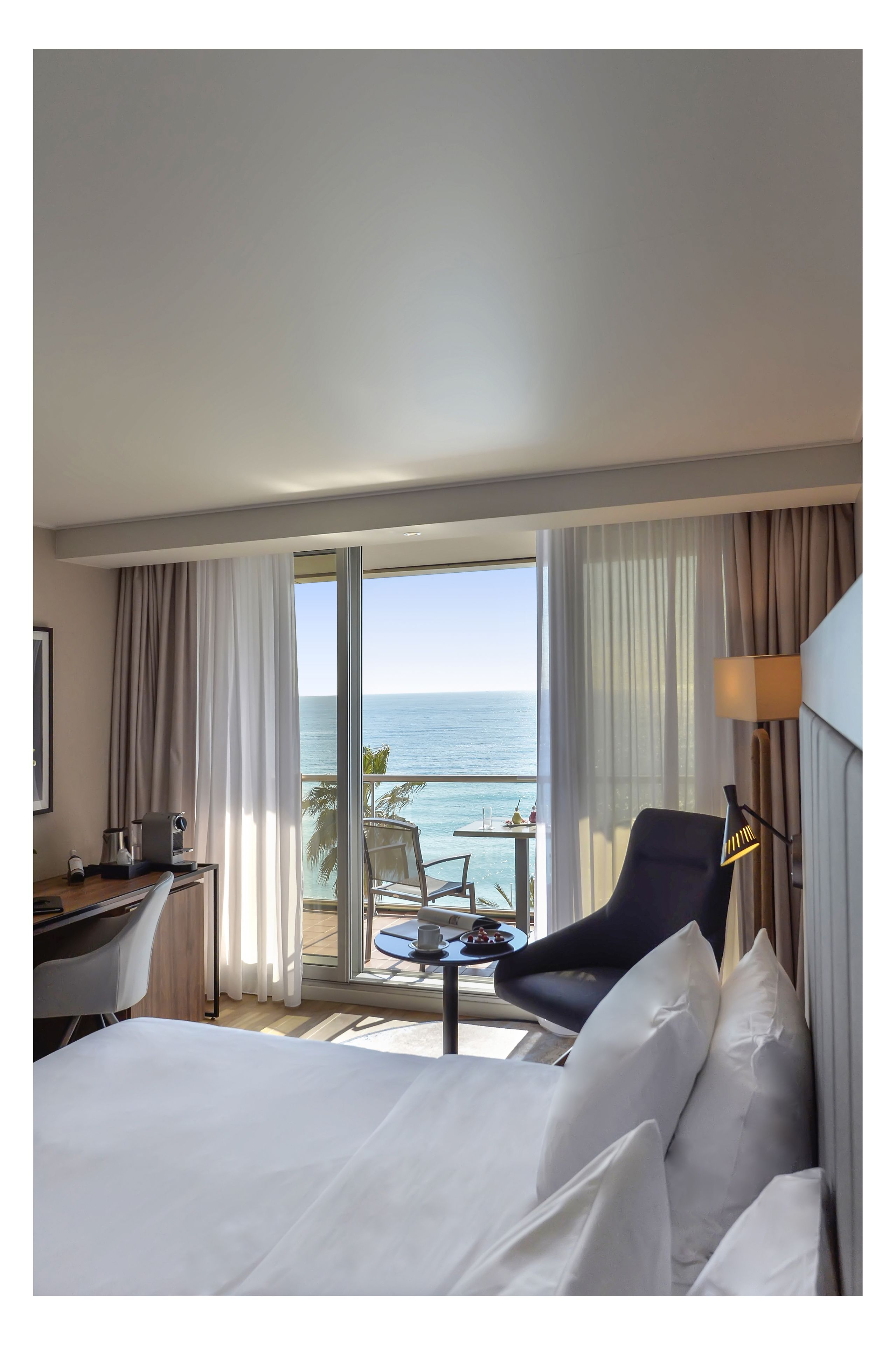 Habitación de hotel con cama, escritorio, silla, lámpara y vista al océano.
