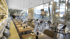 A modern restaurant with a long communal dining area, individual tables, and a view of the ocean.