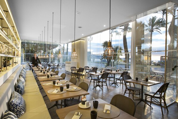 Un restaurante moderno con una amplia zona de comedor común, mesas individuales y vistas al océano.
