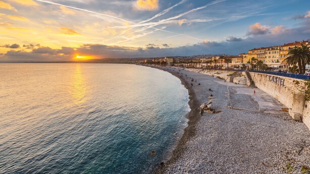 A coastal cityscape with a pebbled beach, a promenade, and historic buildings.