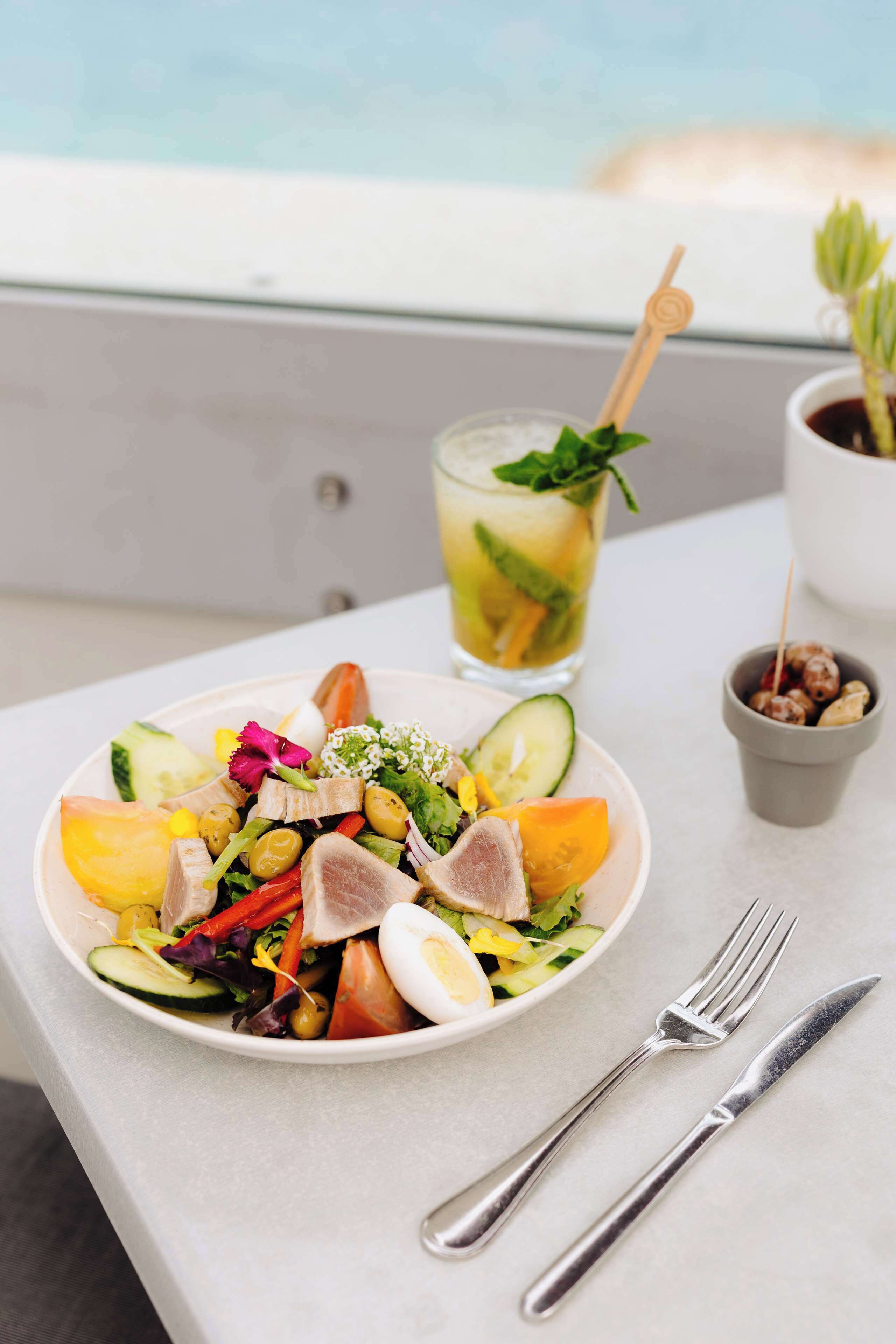 Una mesa con ensalada, una bebida y cubiertos.
