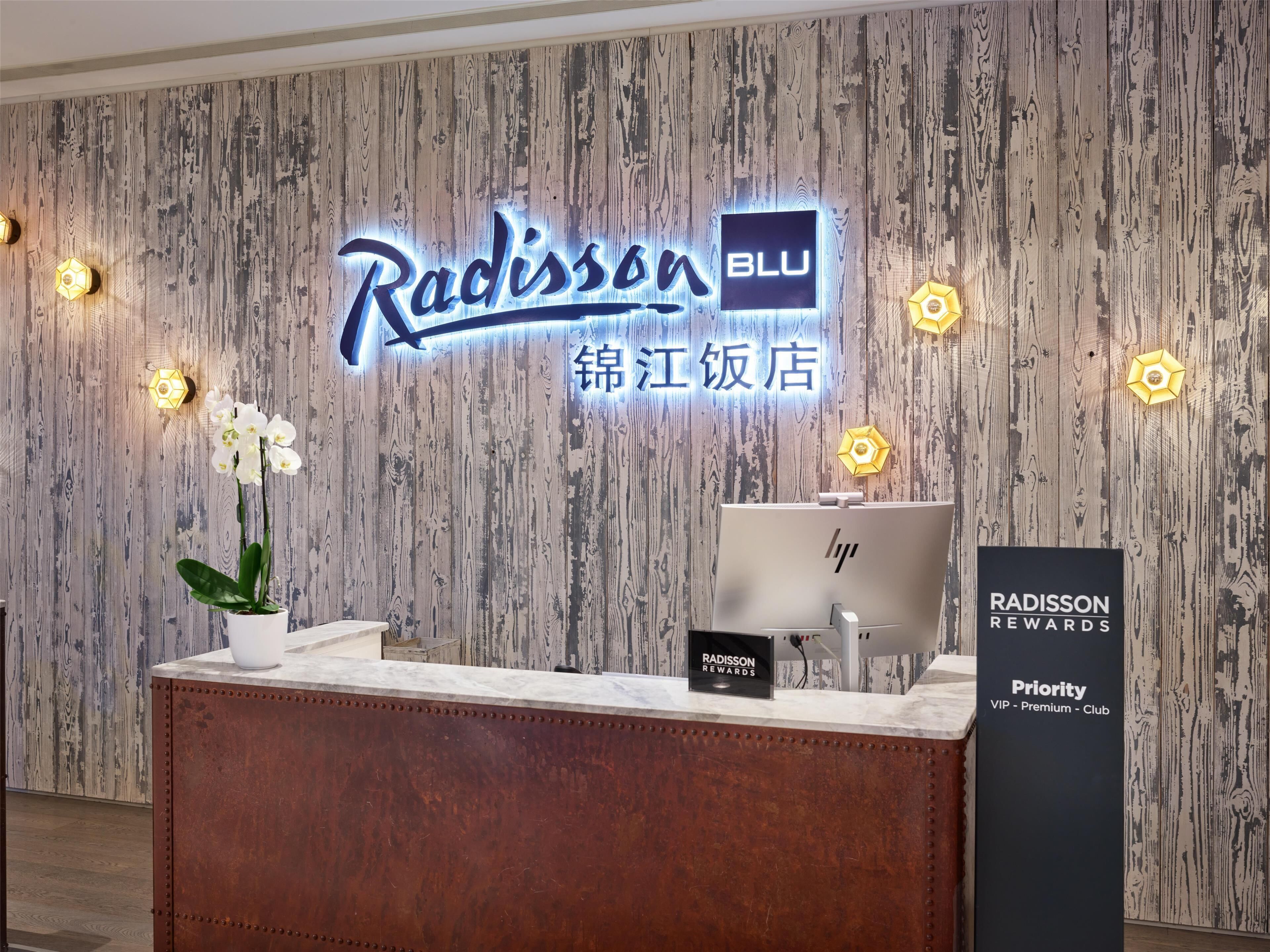 En receptionsdisk med en träpanel som bakgrund, en skylt med texten ”Radisson BLU” och en skylt för ”Radisson Rewards” som visar att det finns ett lojalitetsprogram.
