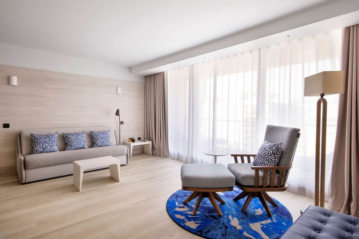 A modern hotel room with a sofa, ottoman, and armchair arranged around a central coffee table.