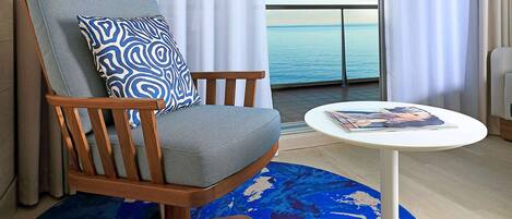 A modern room with a wooden chair, a round table, and a view of the sea through large windows.