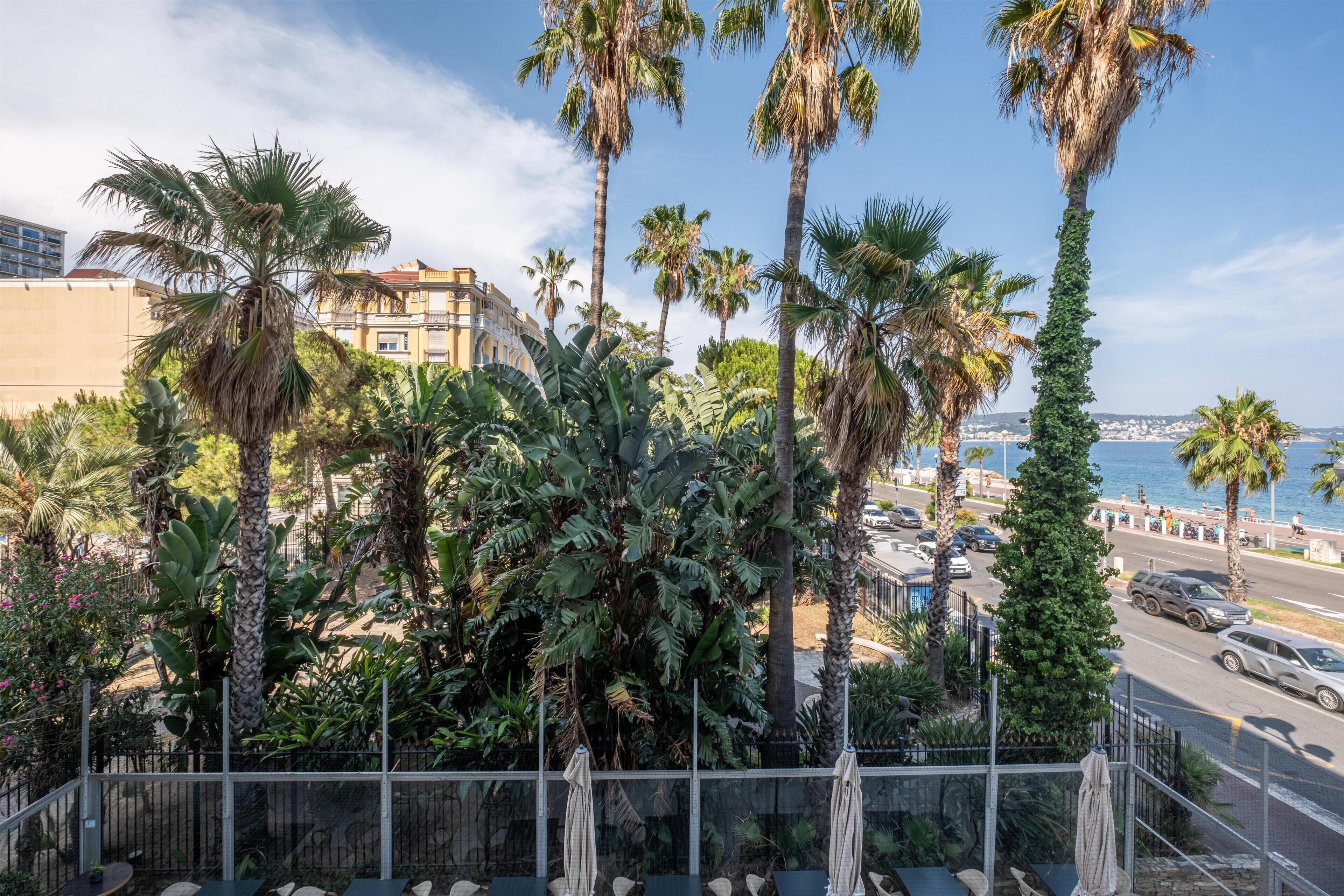 A balcony with a view of a coastal road, palm trees, and a building with balconies.