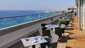A rooftop terrace with tables and chairs, overlooking a coastal view.